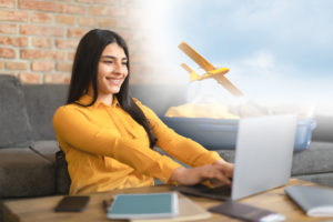 excited spanish lady using laptop and planning trip at home, packing suitcase, booking hotel or flight tickets online