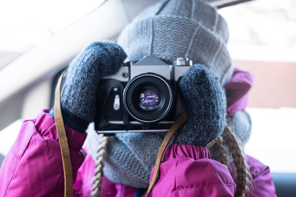 a girl in winter clothes takes a picture with a camera while in the car.